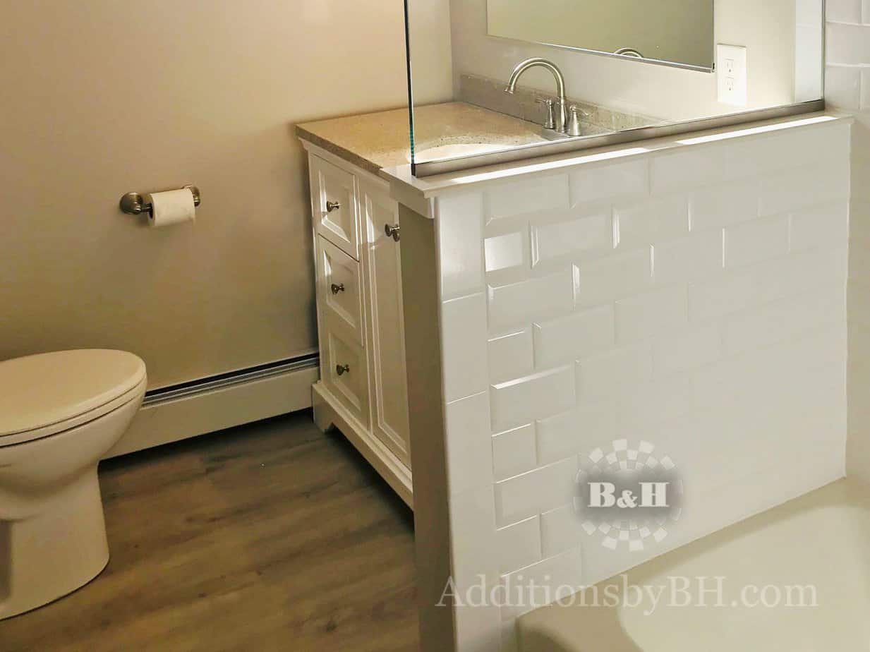A remodeled bathroom with a single sink and partial wall, with our company logo.