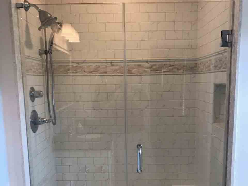 A shower with a glass door and white tiling.
