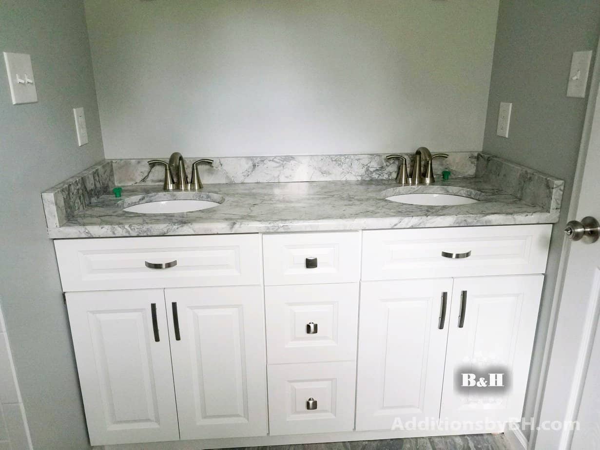 A remodeled bathroom with a double vanity, with our company logo.