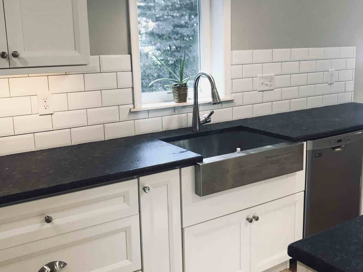 Remodeled kitchen with black counter tops and white tile backsplash.