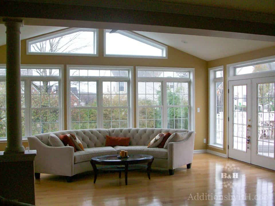 A refinished sunroom home addition with large windows and a curved couch, with our company logo